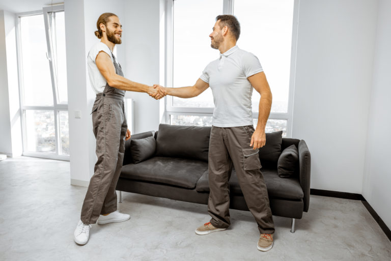 Two happy professional movers or repairmen in workwear shaking hands together, finishing work in the apartment